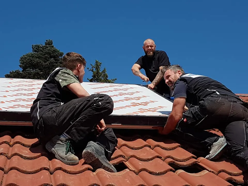 Drei Monteure von Haustechnik Berberich montieren eine Solaranlage auf einem Ziegeldach